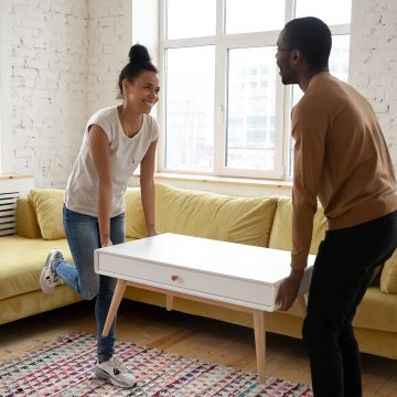 Furnishing home with love. Laughing inspired african american couple of renters, tenants, buyers or owners of apartment carrying and placing furniture indoors, happy black family moving to new house